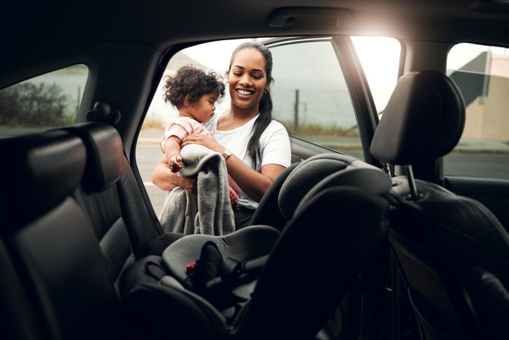 Mother placing baby in a car seat in the back of her car.